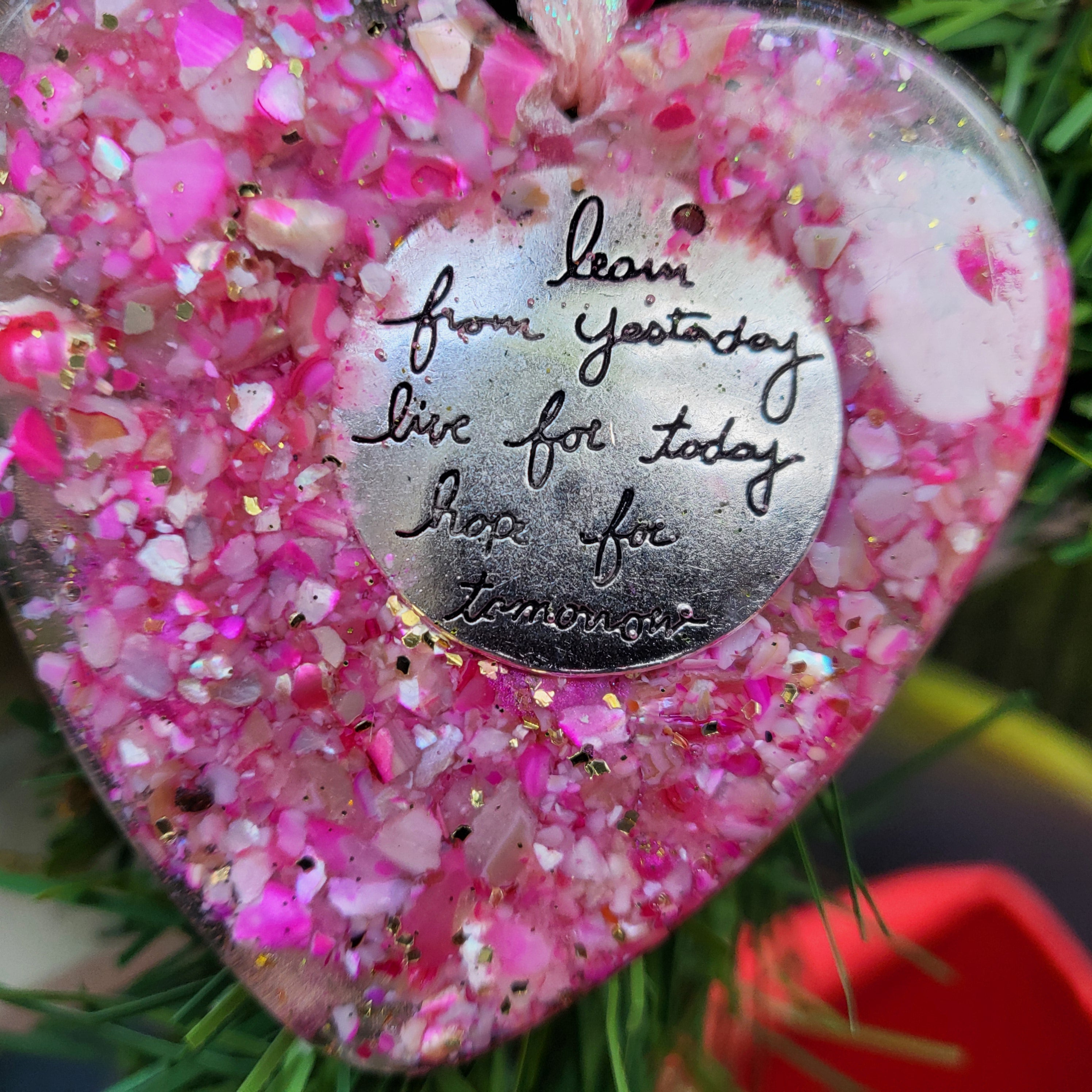 Pink glittery heart ornament with a silver tag on a green background